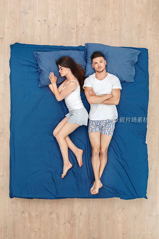 睡觉前。年轻夫妇男人交叉双臂关心而女人睡在床上俯视图
