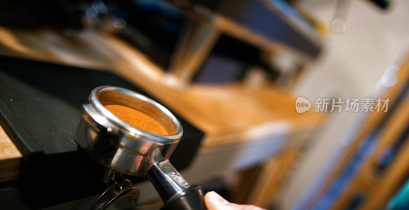 特写镜头的一个新鲜的水平和夯实的咖啡渣在一个门滤，而咖啡师使浓缩在咖啡店