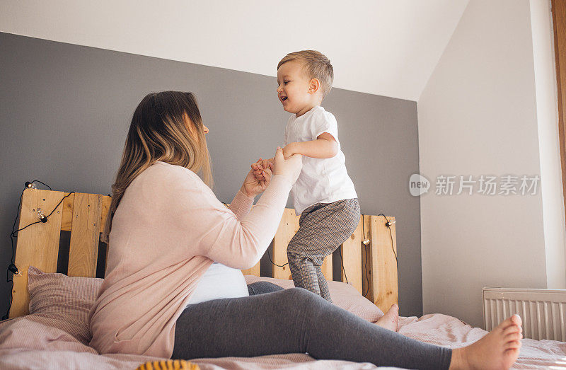 怀孕的妈妈和年幼的儿子在卧室里玩耍