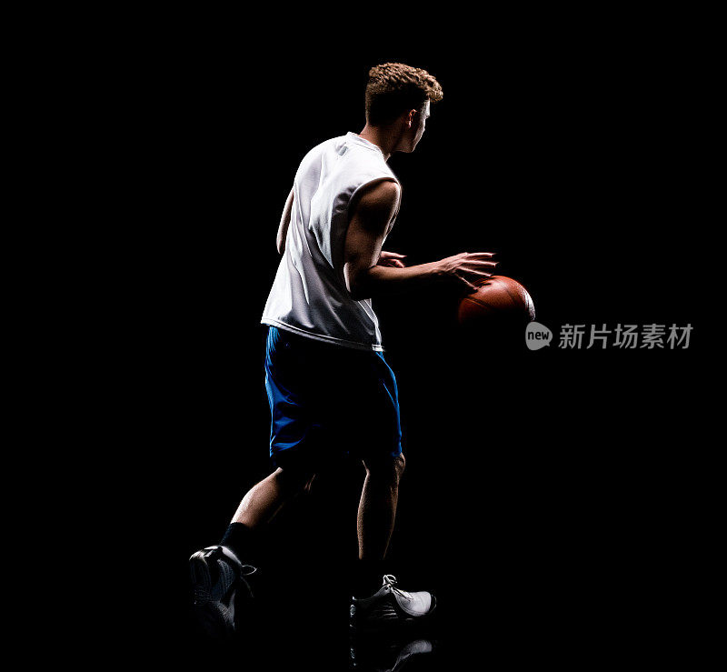 白人男性身穿短裤，手持篮球，使用运动球在黑色背景前无袖奔跑