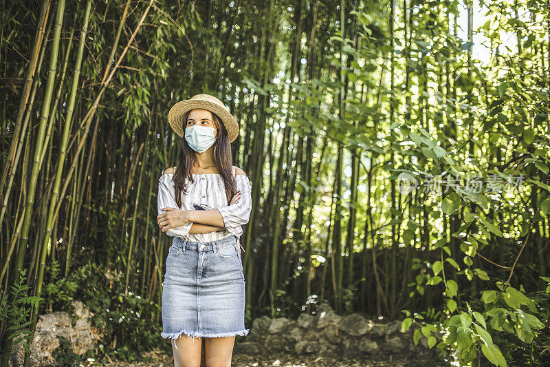 在冠状病毒大流行期间，戴着防护面罩的美丽女子在大自然中度过时光