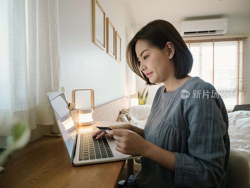 年轻女子在家里放松的时候使用笔记本电脑和信用卡