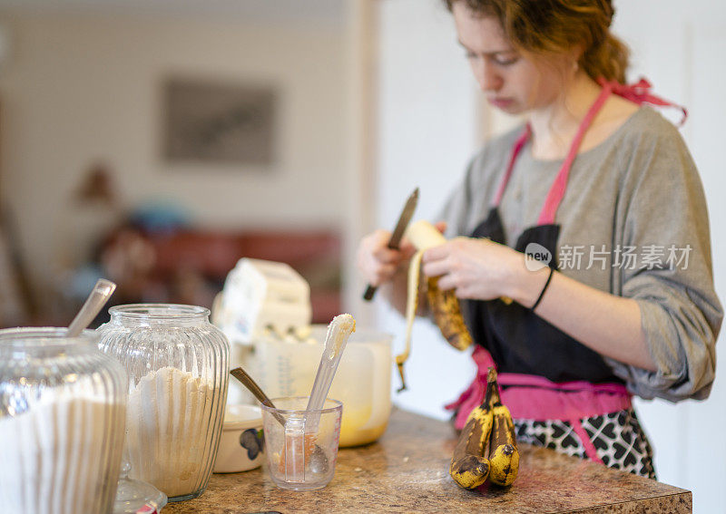 一个年轻女子在家里的厨房里烤香蕉面包，把香蕉切成面糊。