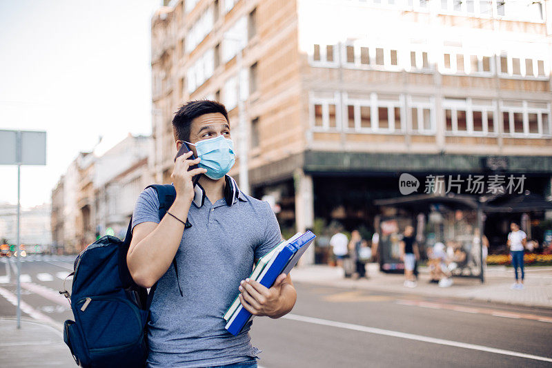 戴着口罩的学生走到学校，正在打电话