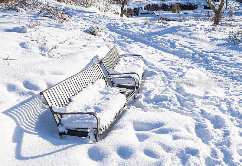 城市公园里的冬天，花园长椅上白雪覆盖。芬兰科特卡市的城市公园。