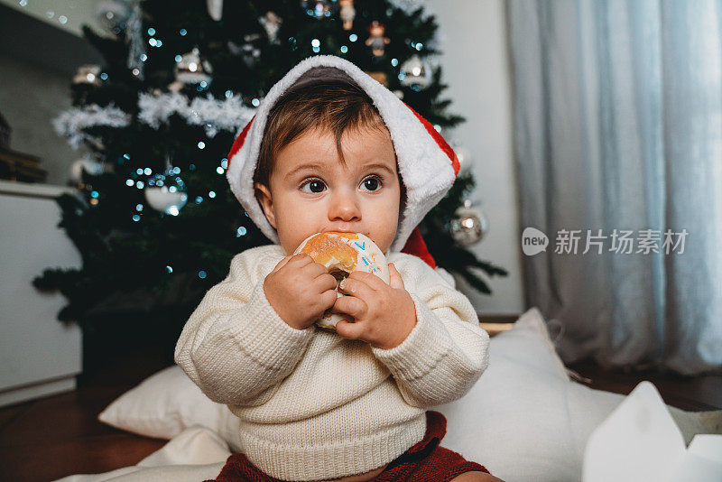 一个小孩在家里的圣诞树旁吃甜甜圈