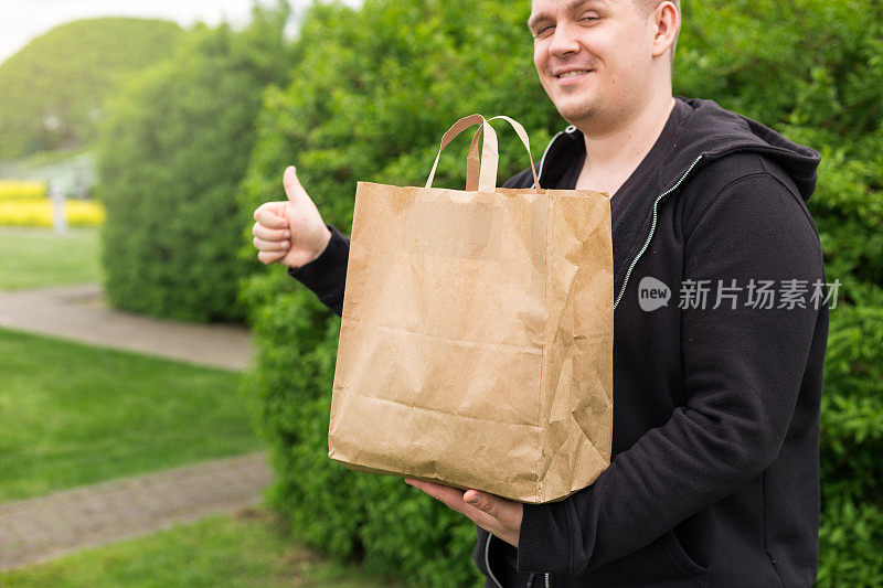 外卖环保纸袋男子对大自然的绿色背景竖起大拇指。在任何天气条件下24小时送货给客户。