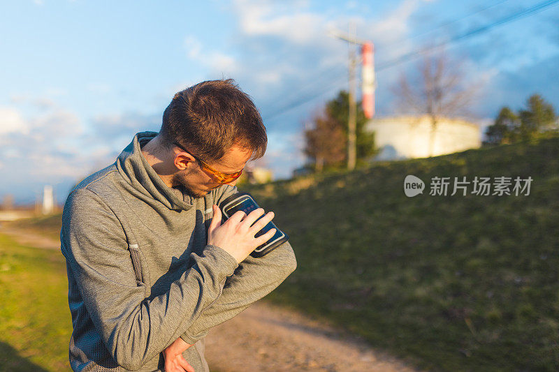 一名年轻男性跑步者在袖标手机壳内使用手机的特写镜头