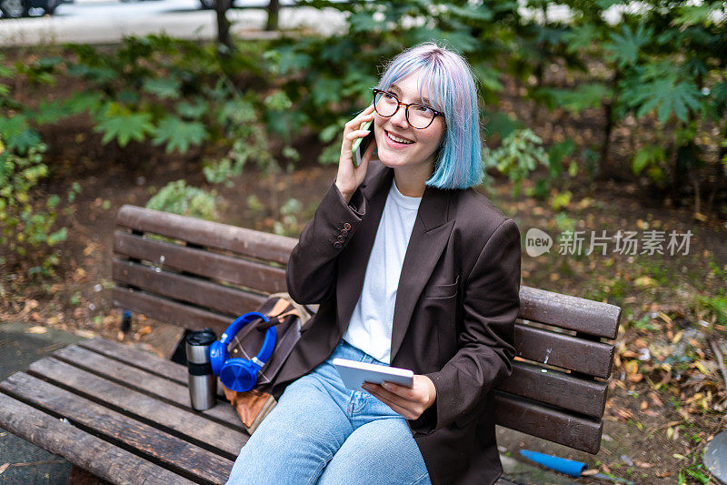 头发鲜艳的年轻企业家在城市里用数字平板电脑和电话检查她的生意