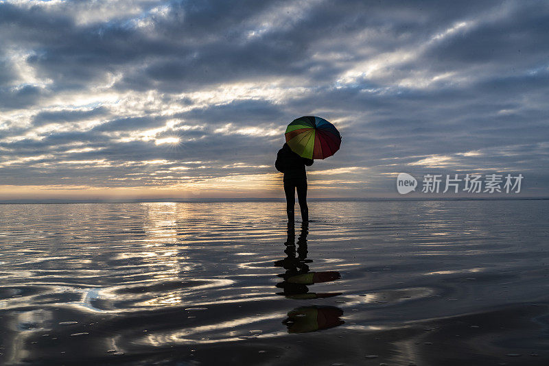 女人撑着雨伞在盐湖风景中看日落