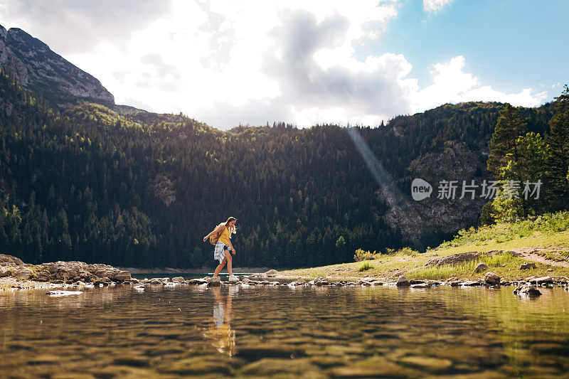 一位女登山运动员穿过一个湖。她背着徒步旅行用的背包。