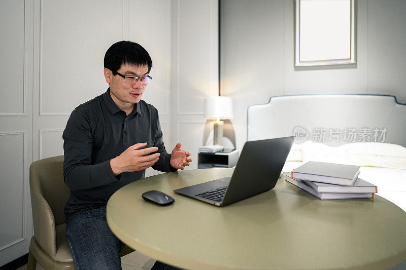一位中年亚洲白领在家里用笔记本电脑进行在线视频会议