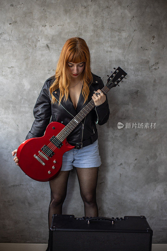 摇滚女孩拿着红色电吉他站在灰色的墙前