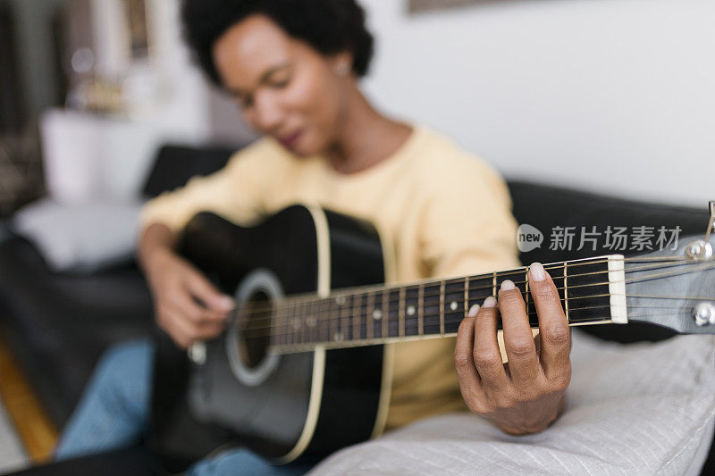 成熟美丽的黑人妇女坐在家里的沙发上弹吉他，微笑和欣喜的特写