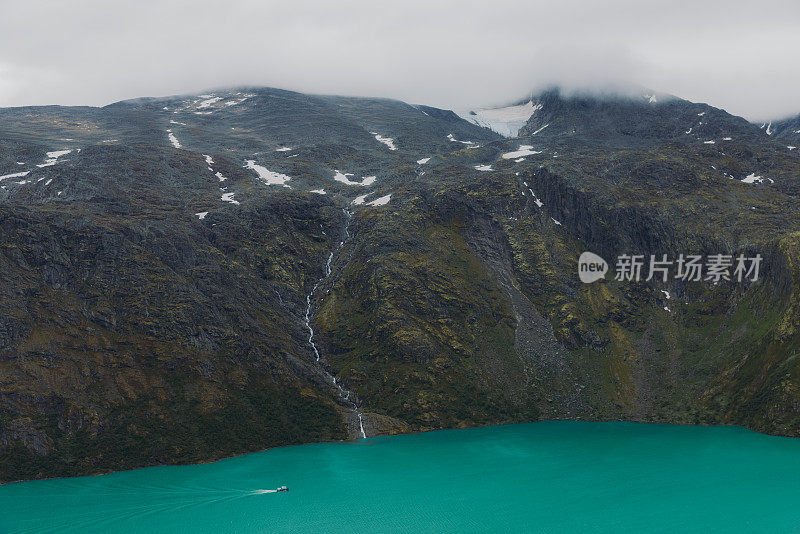 在挪威约顿海门国家公园水晶蓝色的冰川湖上航行的渡轮的戏剧性视图