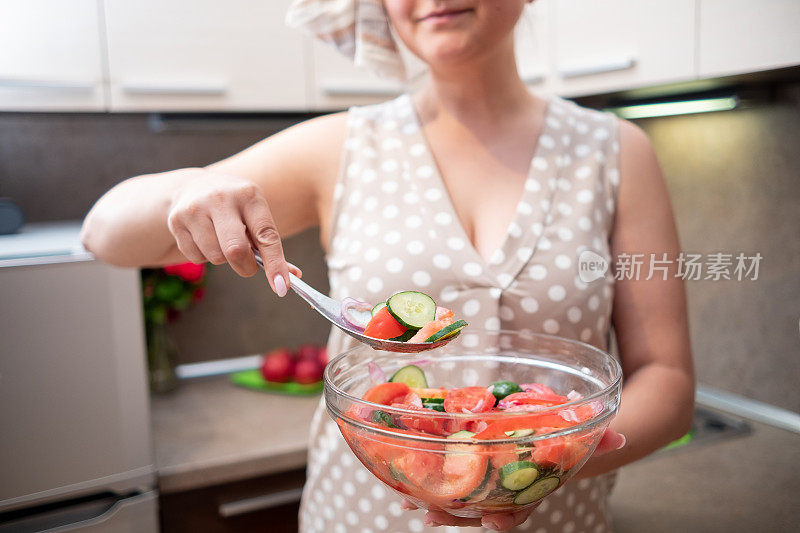 一位穿着棕色衣服的年轻女子在米黄色的厨房里做素食沙拉。