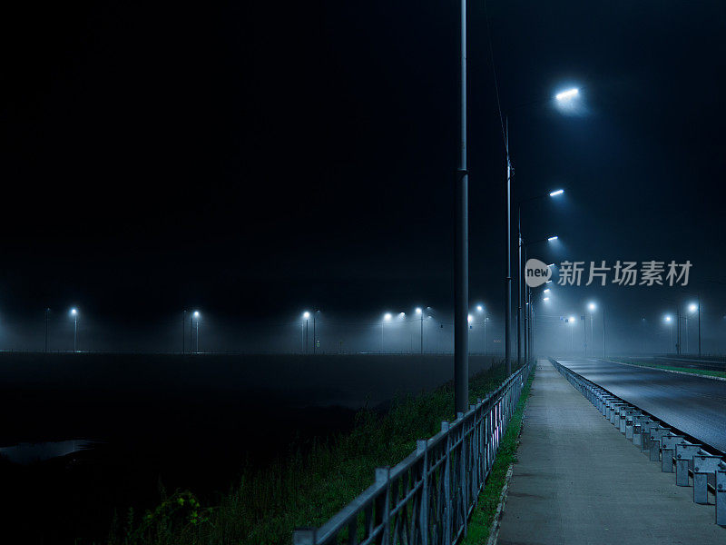 夜晚雾蒙蒙的高速公路被灯柱照亮。秋天雾蒙蒙的景观