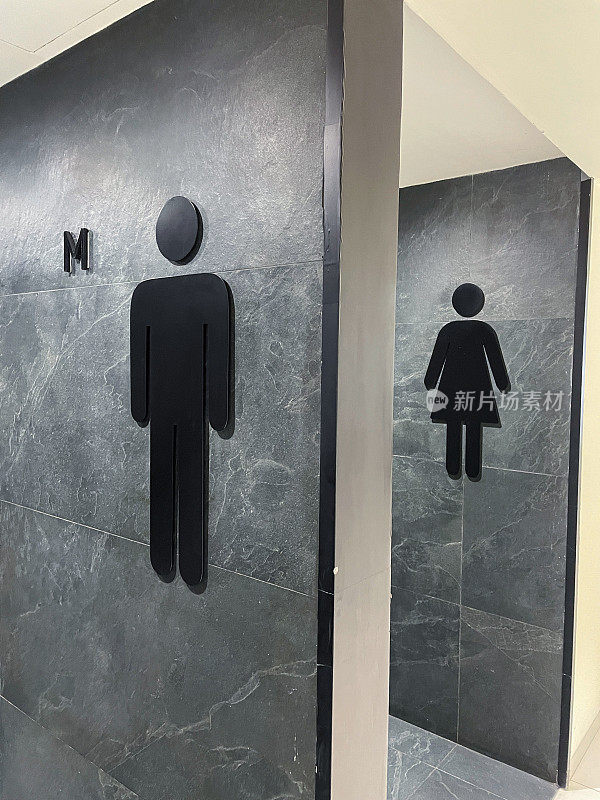 现代公共厕所墙的标志形象，黑色，男性(绅士)和女性(女士)符号在灰色，大理石效果瓷砖公共厕所墙