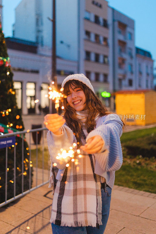 美丽的年轻女子拿着烟花在户外的一棵大圣诞树前