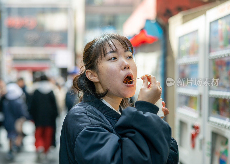 年轻女游客在街上吃韩国小吃