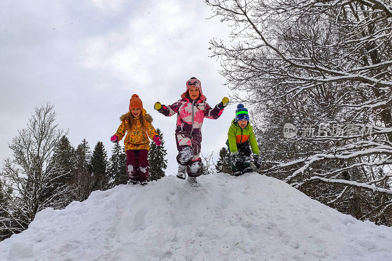 三个孩子是白种人，兴高采烈地从一堆雪上跳下来。