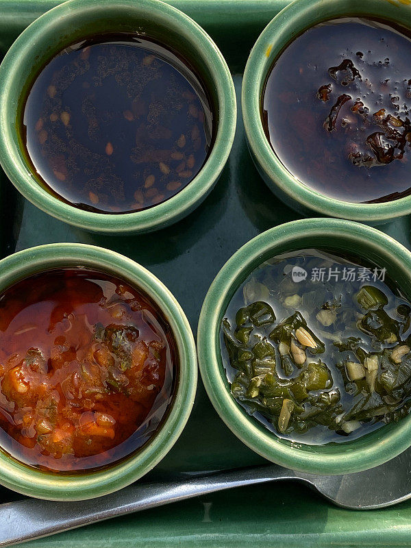 绿色方形盘子的特写图片，有四种蘸酱，用于圆形模子中的饺子，辣椒油，酱油，西红柿和大蒜辛辣调味品，高架俯视