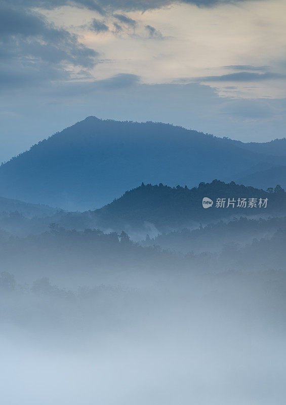 这是一幅宁静的图像，一个雾蒙蒙的山谷，层层叠叠的小山逐渐消失在远处，周围是宁静的气氛和微妙的橙色和蓝色