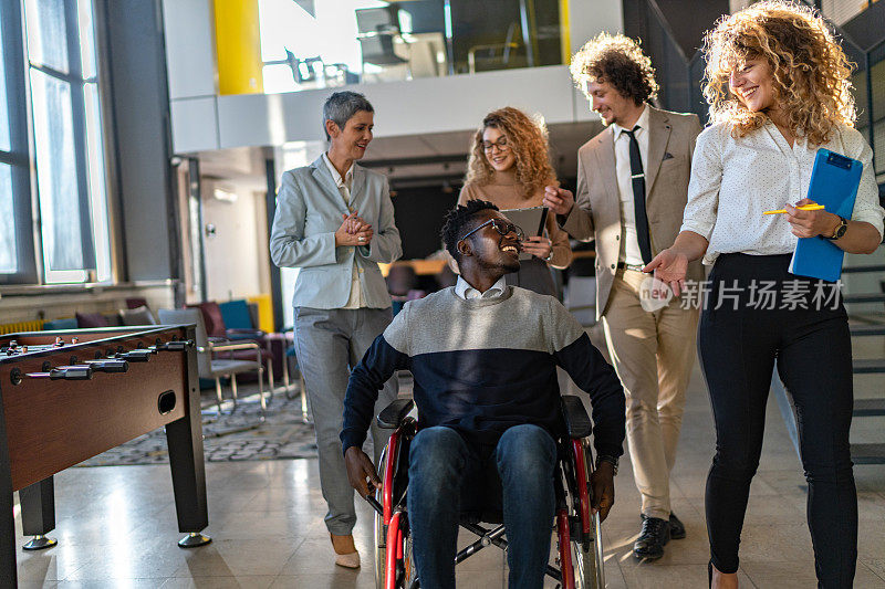 坐在轮椅上的白领男员工和他的女同事在人行道走廊上愉快地交谈