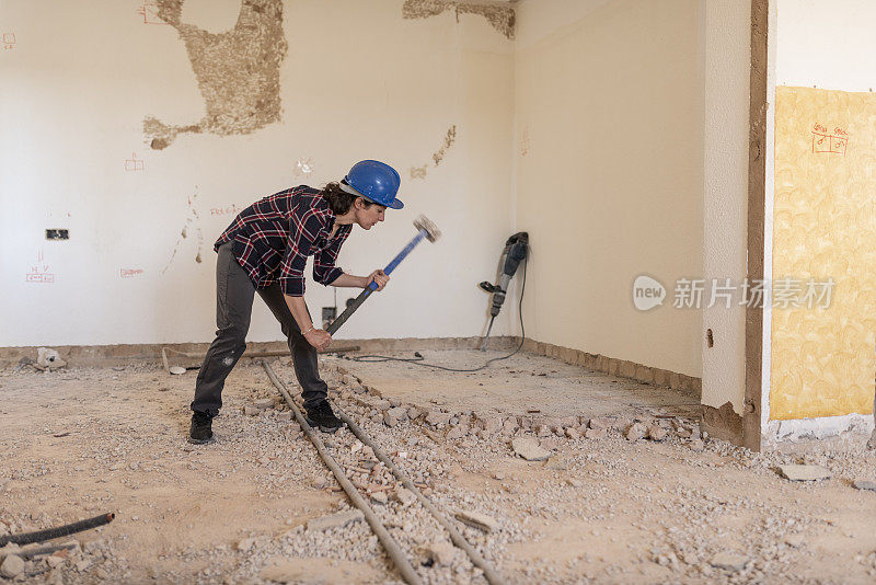 在建筑装修期间，一名妇女拿着沉重的拆除锤敲打地面