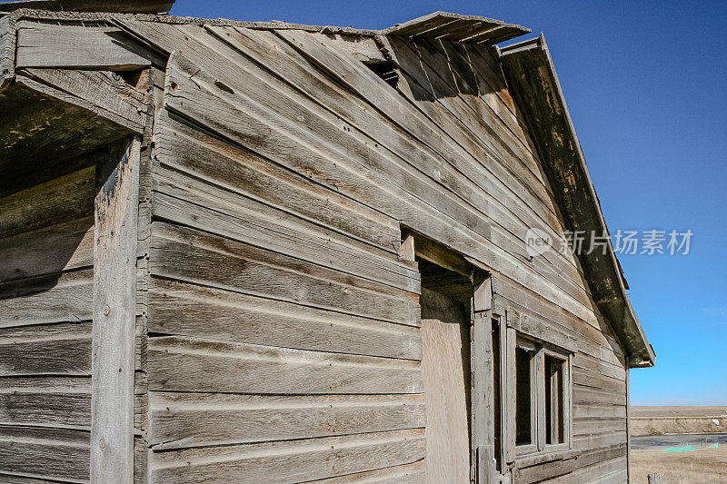 一扇边界门的外部，两扇空的破窗户和悬在废弃的旧木结构建筑上的保护性屋顶