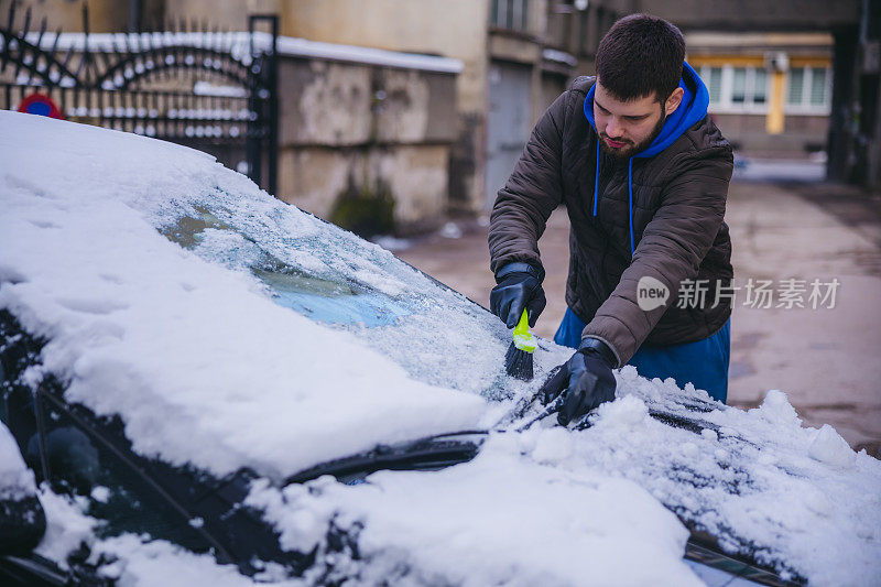 年轻人正在清除汽车上的积雪