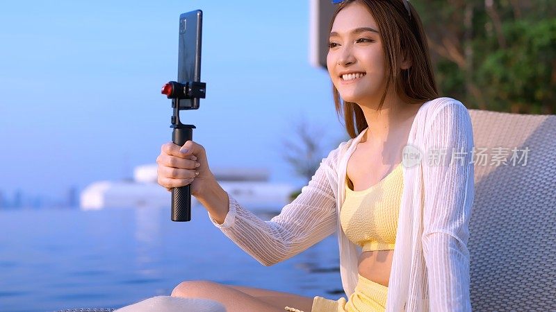 夏季休闲休闲亚洲女性黄色比基尼享受视频通话与她的朋友通过智能手机亚洲网红广播生活方式分享经验与她的追随者在社会