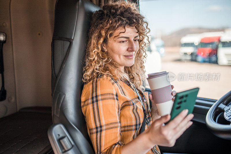 女卡车司机在开车休息时用手机上网，用一次性杯子喝咖啡