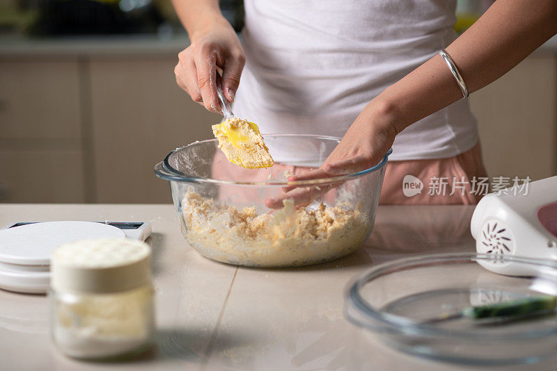 一名妇女在家里的厨房里，用糖、打好的鸡蛋、黄油和面粉混合椰子饼干的配料