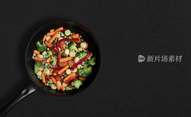 煎锅与切片冷冻蔬菜混合在黑色背景。蔬菜混合沙拉。俯视图，平铺。副本的空间。