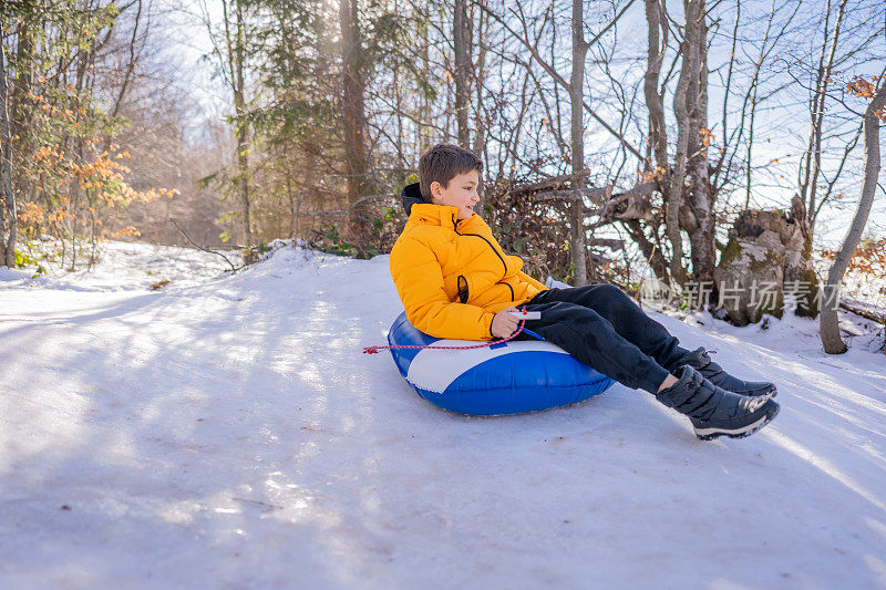 小男孩骑着雪管从山上滑下来