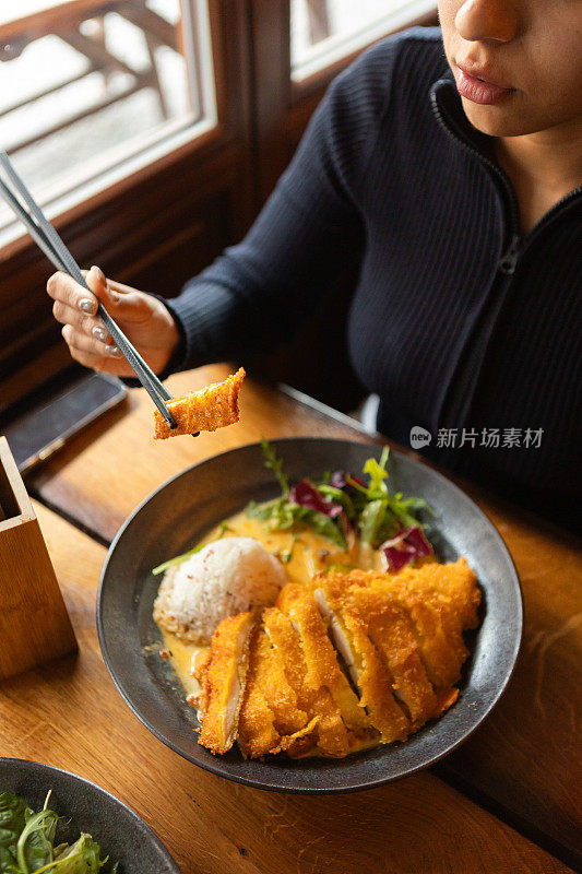 年轻女子在餐厅里吃着越南菜，配上蔬菜、鸡肉和咖喱酱米饭