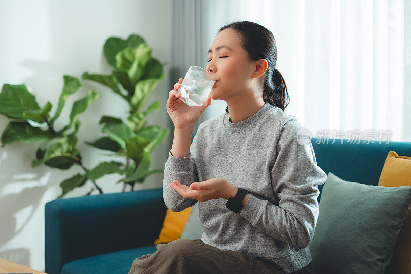 一个亚洲女人坐在客厅的沙发上喝凉水休息。