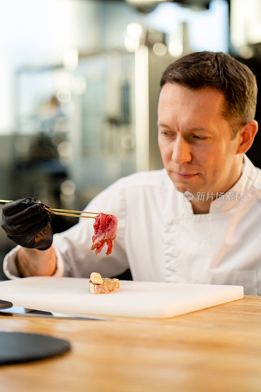 戴着黑色手套的厨师用镊子夹一块生腌肉块法棍面包的脸部特写
