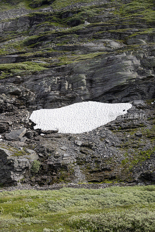 最后的积雪在七月的阳光下逐渐融化，在通往1500米高的Geirangerfjord天空步道的挪威山边。