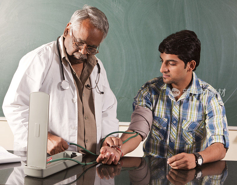一位印度教授正在给一个年轻人测量血压。