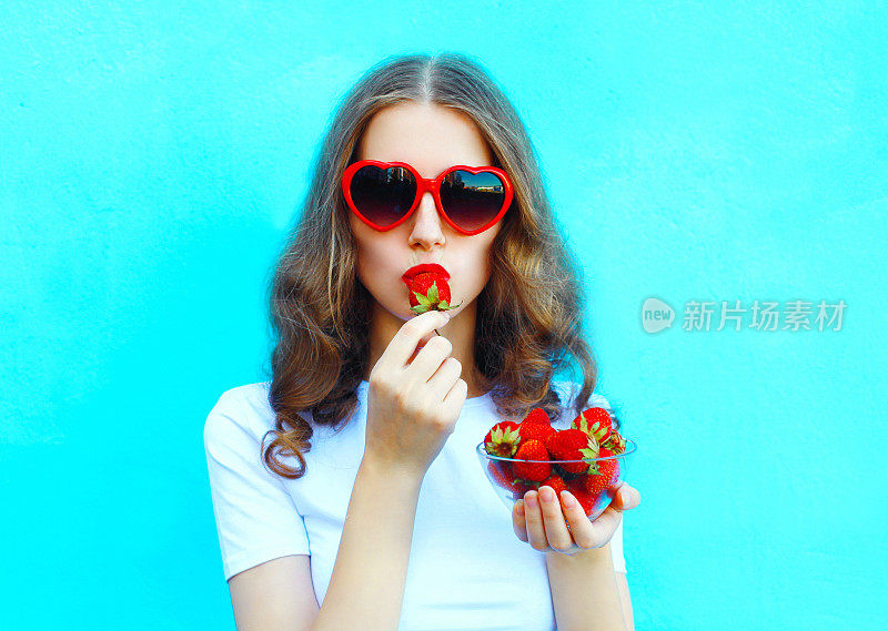 肖像漂亮的女人与许多草莓在彩色的蓝色