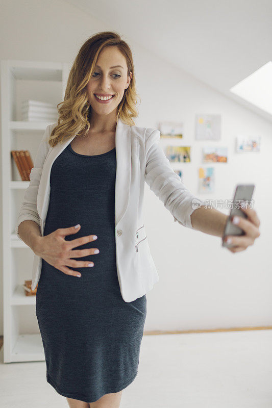 怀孕女商人用智能手机自拍。