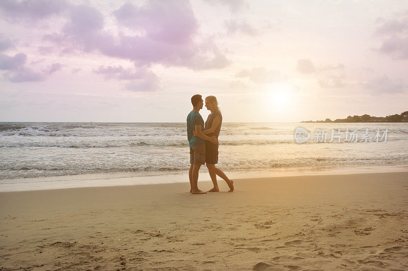 一对美丽的情侣在日落海滩上互相拥抱，深情对视。