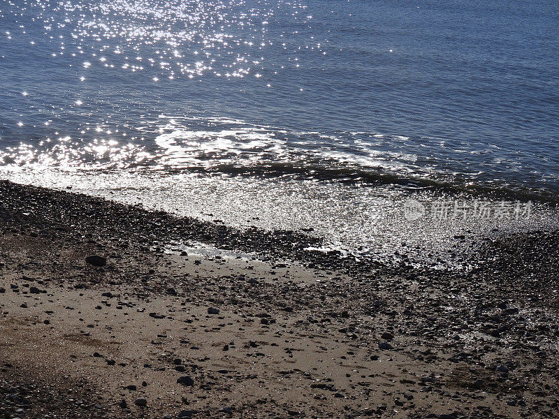 在强烈的阳光下波光粼粼的大海，卵石海滩和海边的形象