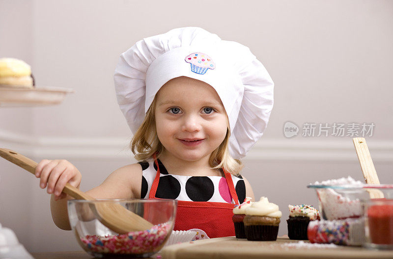 小女孩戴着厨师帽和围裙装饰纸杯蛋糕