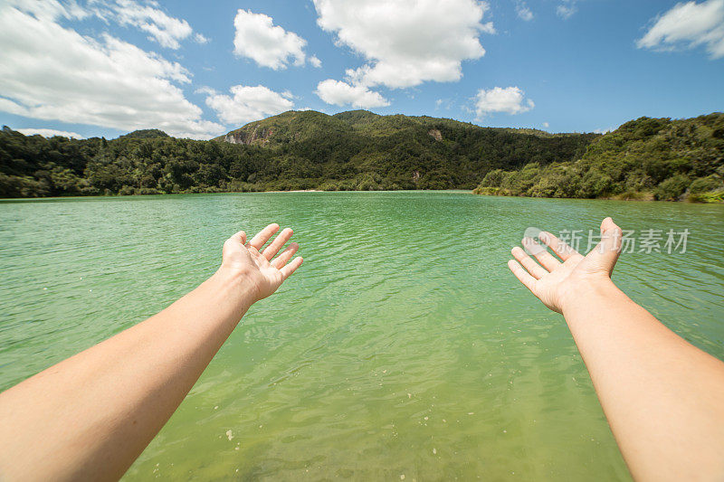 在新西兰，女人的双臂伸向绿色的湖泊