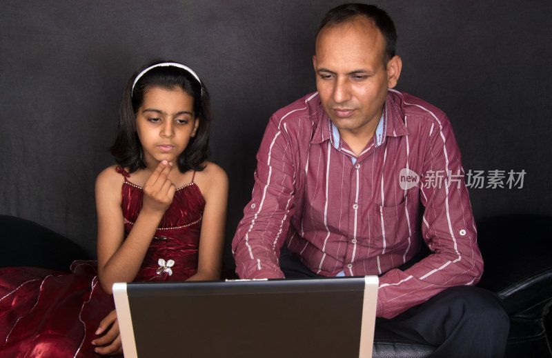 快乐的印度女孩拿着笔记本电脑和她的父亲