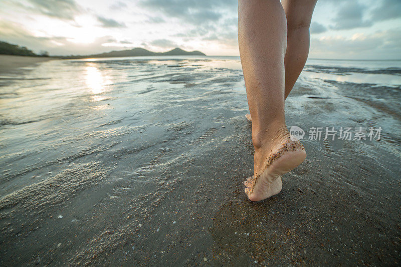 在太阳升起时赤脚在海滩上行走的特写