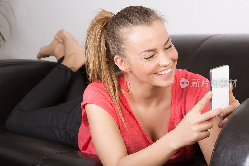一个在沙发上拿着手机的快乐年轻女人